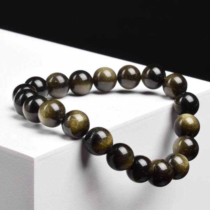 Bracelet obsidienne dorée perles 8 mm posé sur un cube blanc