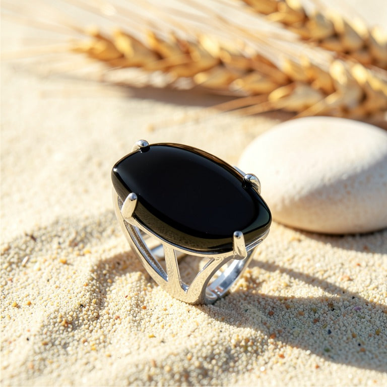 Bague Onyx Noir réglable en métal argenté, cabochon marquise, posée sur le sable